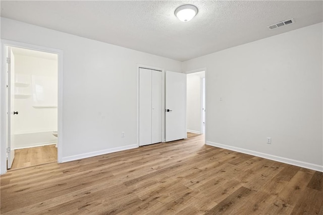 unfurnished bedroom with visible vents, baseboards, wood finished floors, a closet, and a textured ceiling