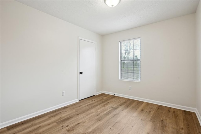 unfurnished room featuring a textured ceiling, light wood-type flooring, and baseboards