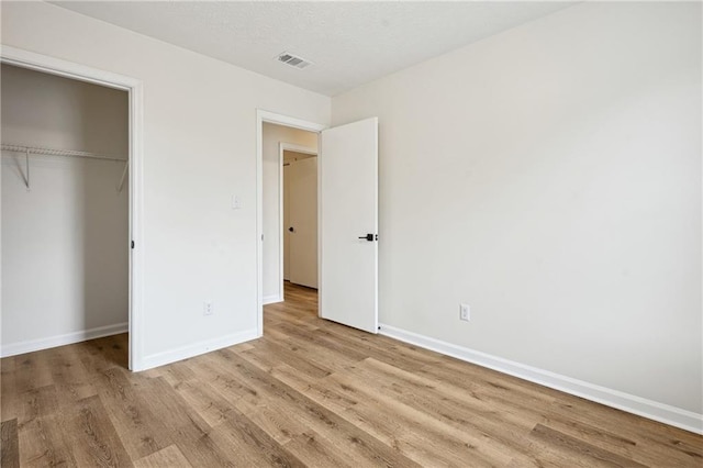 unfurnished bedroom featuring wood finished floors, visible vents, baseboards, a closet, and a textured ceiling