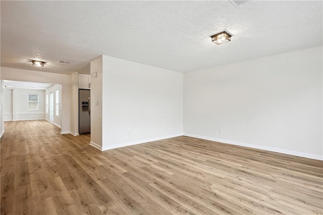 spare room with light wood-type flooring, baseboards, and a textured ceiling