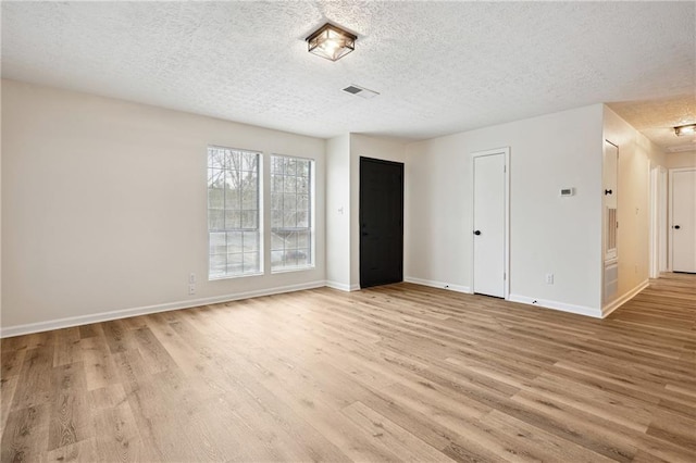 spare room with light wood finished floors, visible vents, a textured ceiling, and baseboards