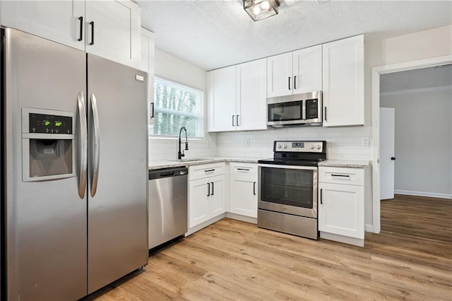 kitchen with a sink, light wood-type flooring, appliances with stainless steel finishes, and white cabinets