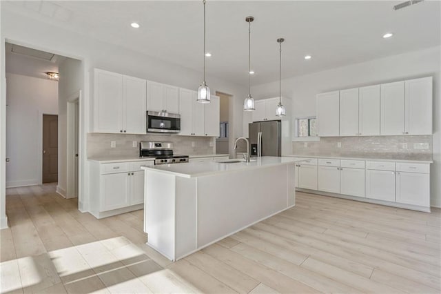 kitchen featuring an island with sink, light countertops, appliances with stainless steel finishes, white cabinets, and a sink