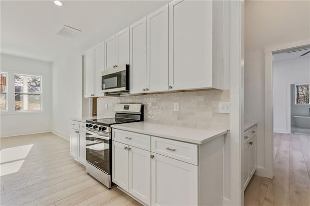 kitchen featuring decorative backsplash, light countertops, light wood finished floors, and appliances with stainless steel finishes