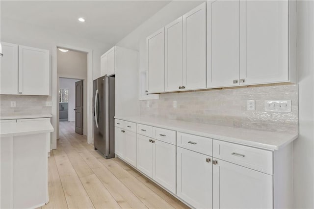 kitchen featuring light wood-type flooring, backsplash, freestanding refrigerator, white cabinets, and light countertops