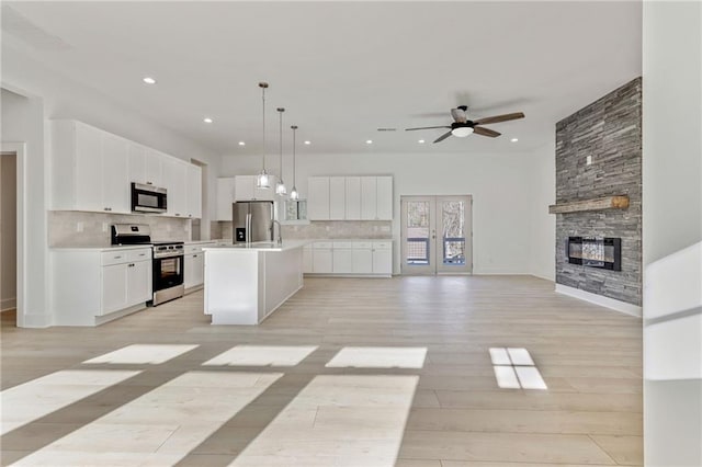 kitchen featuring backsplash, appliances with stainless steel finishes, open floor plan, and an island with sink