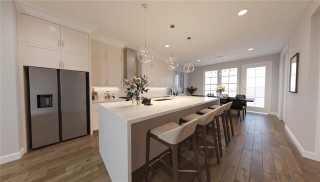 kitchen featuring a kitchen island with sink, stainless steel refrigerator with ice dispenser, and white cabinets