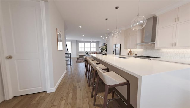 kitchen with wall chimney exhaust hood, a breakfast bar, pendant lighting, white cabinets, and light hardwood / wood-style floors