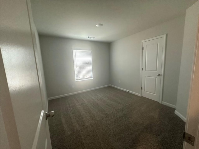 spare room featuring dark carpet, baseboards, and visible vents
