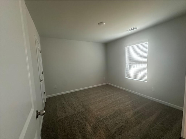 spare room with baseboards, visible vents, and dark colored carpet