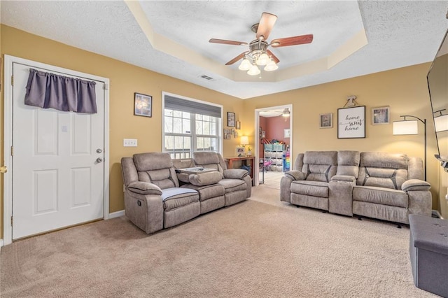 carpeted living area featuring visible vents, a textured ceiling, a raised ceiling, and a ceiling fan