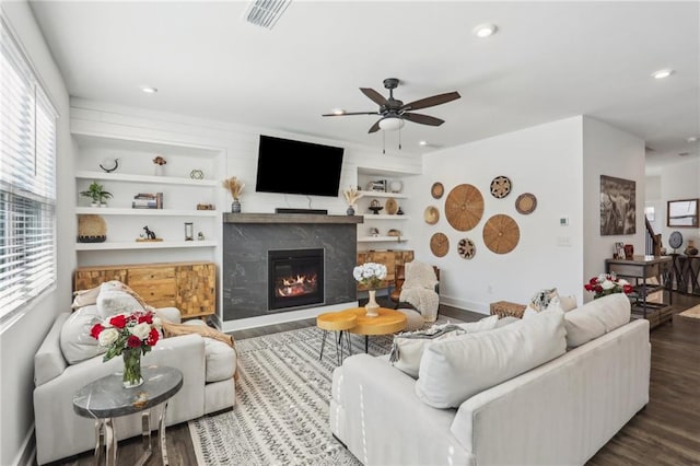 living room featuring built in features, a ceiling fan, wood finished floors, visible vents, and a fireplace