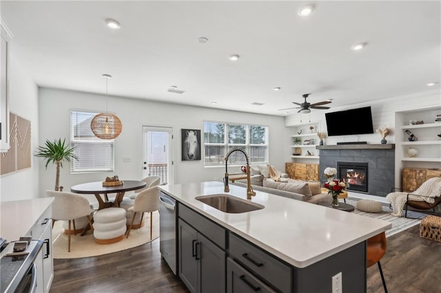 kitchen with a glass covered fireplace, a ceiling fan, a sink, dark wood-type flooring, and stainless steel dishwasher