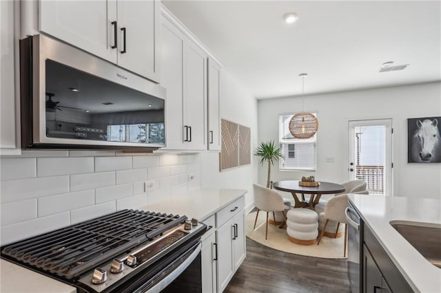 kitchen featuring dark wood-type flooring, tasteful backsplash, stainless steel appliances, white cabinets, and light countertops