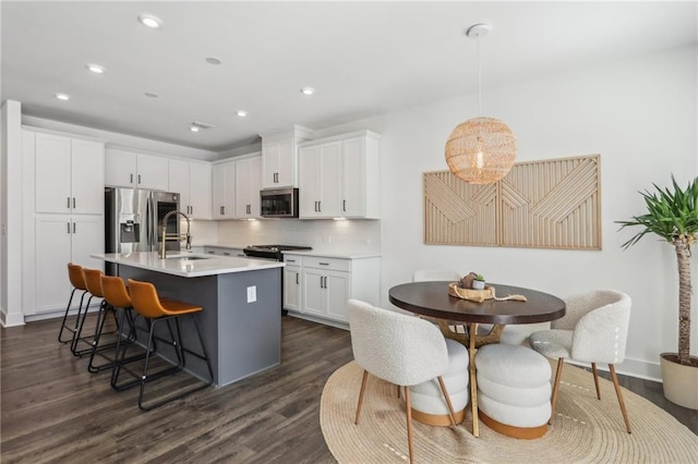 kitchen with a breakfast bar, a sink, dark wood-style floors, white cabinetry, and appliances with stainless steel finishes