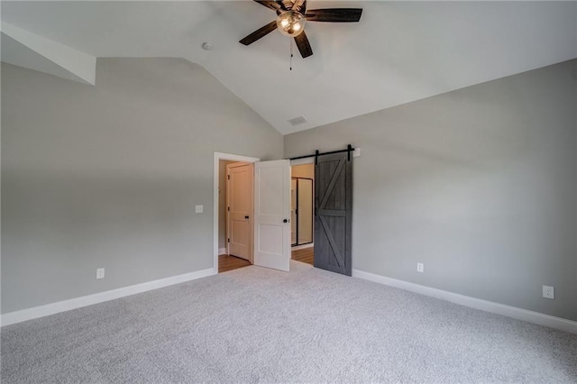 unfurnished bedroom with ceiling fan, a barn door, lofted ceiling, and light carpet