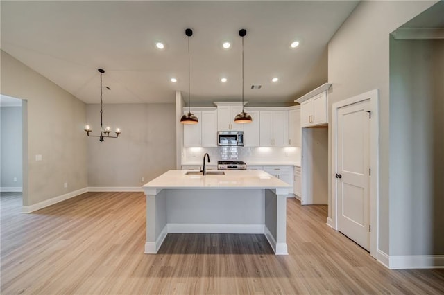 kitchen with white cabinets, sink, hanging light fixtures, an island with sink, and a chandelier