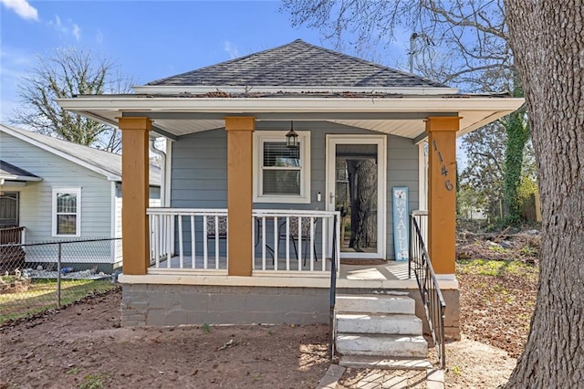 rear view of house featuring a porch, a shingled roof, and fence