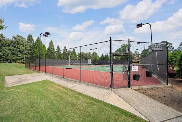 view of tennis court with a lawn, a gate, and fence