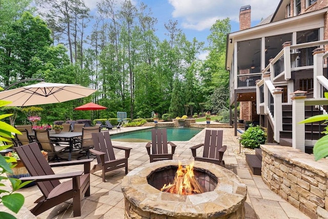 outdoor pool with a patio, a sunroom, and an outdoor fire pit