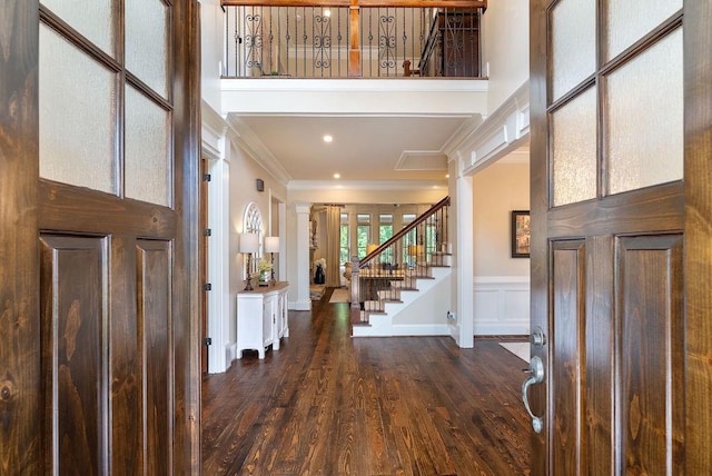 foyer entrance with decorative columns, crown molding, wainscoting, dark wood finished floors, and stairs