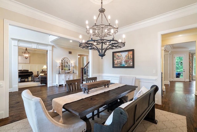 dining space featuring an inviting chandelier, ornamental molding, a decorative wall, and wood finished floors