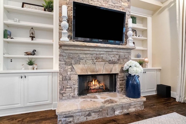 living area with a stone fireplace, dark wood-style floors, and built in features
