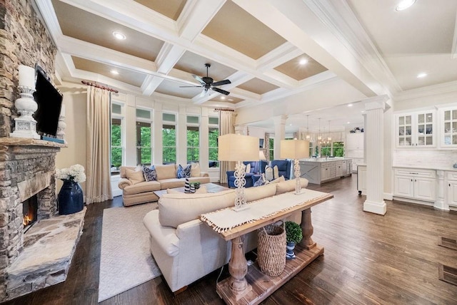 living room featuring a stone fireplace, decorative columns, and dark wood finished floors