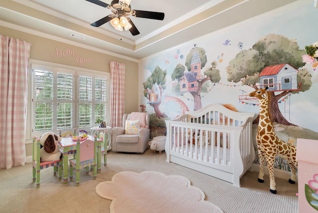 carpeted bedroom featuring a ceiling fan, visible vents, a nursery area, a raised ceiling, and ornamental molding