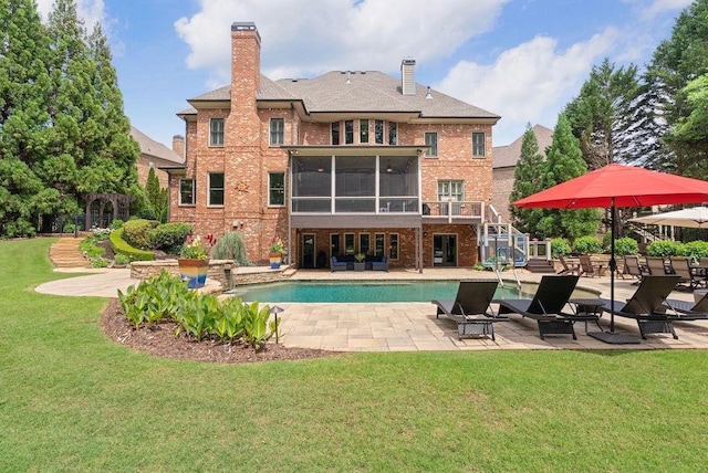 rear view of property featuring a patio, an outdoor pool, brick siding, a sunroom, and a lawn
