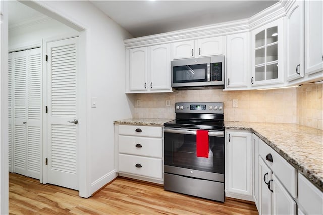 kitchen featuring tasteful backsplash, appliances with stainless steel finishes, glass insert cabinets, light wood-type flooring, and white cabinetry