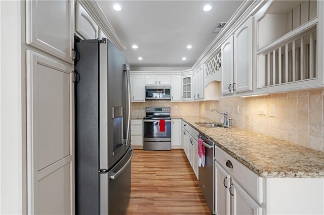 kitchen featuring white cabinets, decorative backsplash, appliances with stainless steel finishes, light wood-style floors, and a sink