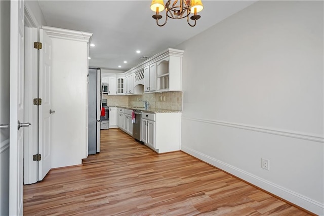 kitchen featuring decorative backsplash, appliances with stainless steel finishes, light stone countertops, light wood-type flooring, and a notable chandelier