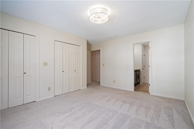 unfurnished bedroom featuring baseboards, carpet flooring, connected bathroom, and multiple closets