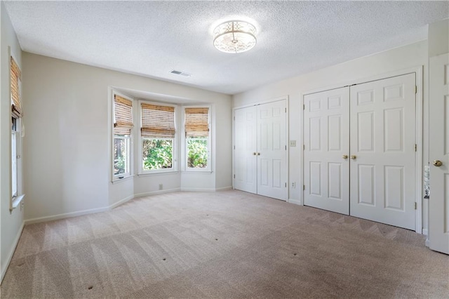 unfurnished bedroom with carpet floors, two closets, visible vents, a textured ceiling, and baseboards