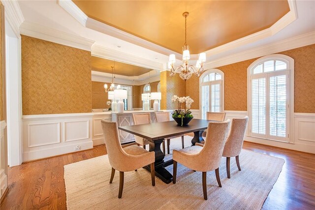 dining area featuring light wood-type flooring, a tray ceiling, an inviting chandelier, and crown molding