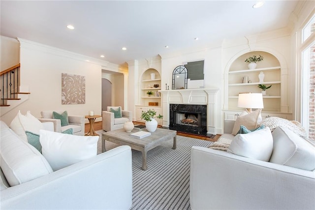 living room featuring built in shelves, hardwood / wood-style flooring, a high end fireplace, and crown molding