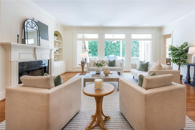 living room featuring light wood-type flooring, built in features, crown molding, and a premium fireplace