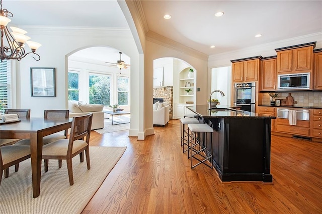 kitchen featuring a kitchen bar, stainless steel appliances, light hardwood / wood-style floors, decorative backsplash, and an island with sink