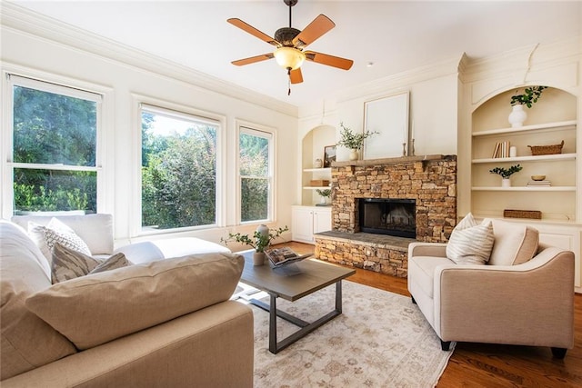 living room with built in shelves, wood-type flooring, crown molding, and a fireplace