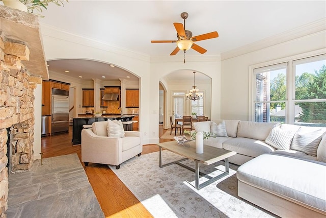 living room featuring light wood-type flooring, ceiling fan with notable chandelier, and crown molding