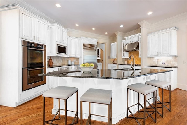 kitchen with light hardwood / wood-style floors, a spacious island, built in appliances, tasteful backsplash, and white cabinetry