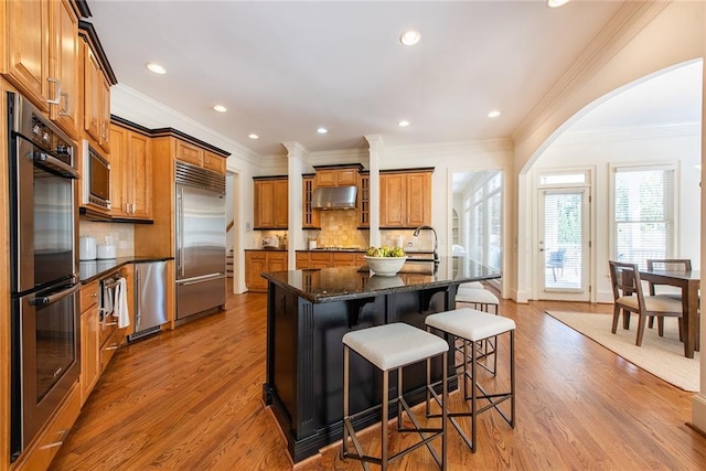 kitchen with built in appliances, light wood-type flooring, a center island, and tasteful backsplash