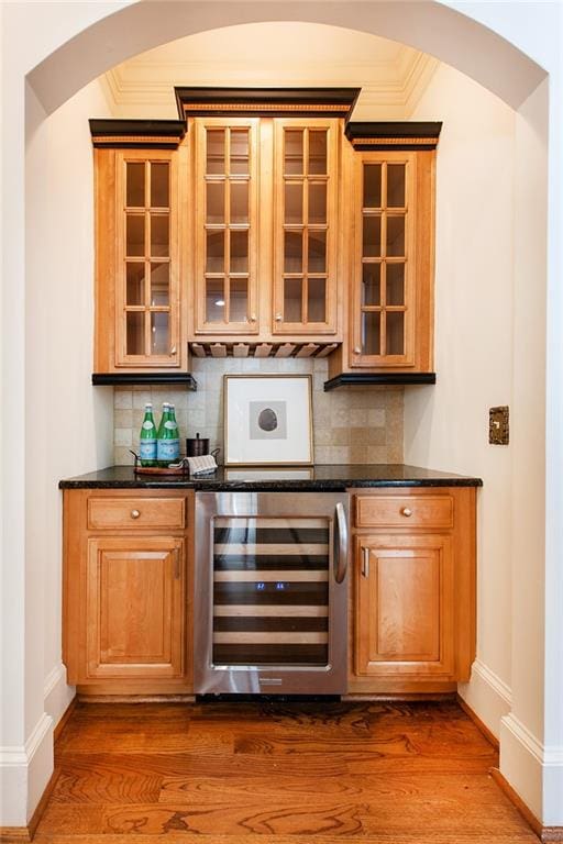 bar featuring dark wood-type flooring, beverage cooler, dark stone counters, and decorative backsplash