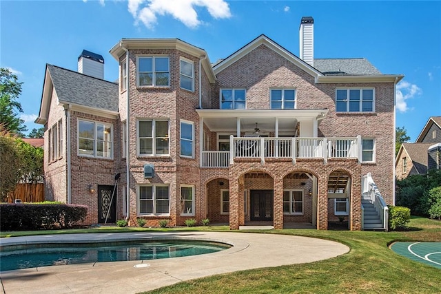 back of house featuring ceiling fan, a balcony, and a yard