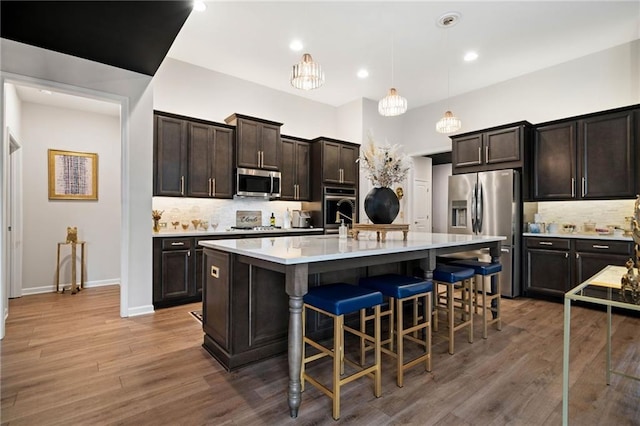 kitchen featuring a breakfast bar, light countertops, decorative backsplash, wood finished floors, and stainless steel appliances