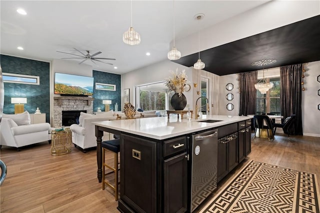 kitchen featuring a sink, light countertops, a stone fireplace, light wood-style floors, and dark cabinets