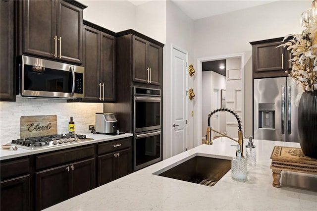 kitchen with light stone counters, backsplash, appliances with stainless steel finishes, and a sink