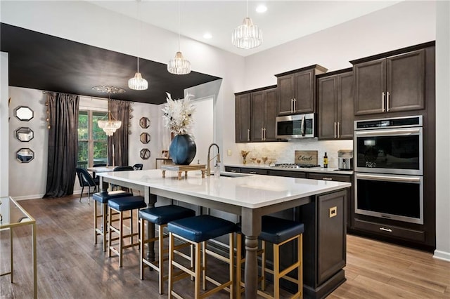 kitchen featuring light wood-type flooring, a sink, appliances with stainless steel finishes, a breakfast bar area, and dark brown cabinets