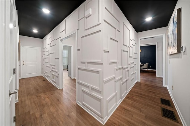 hall featuring dark wood-style floors, visible vents, and baseboards